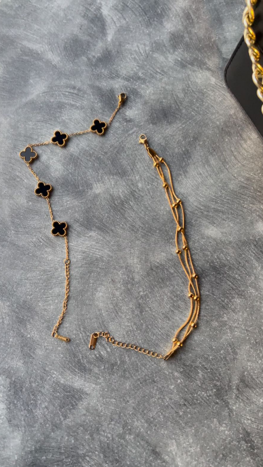Gold chain necklace with black clover pendants on a gray surface