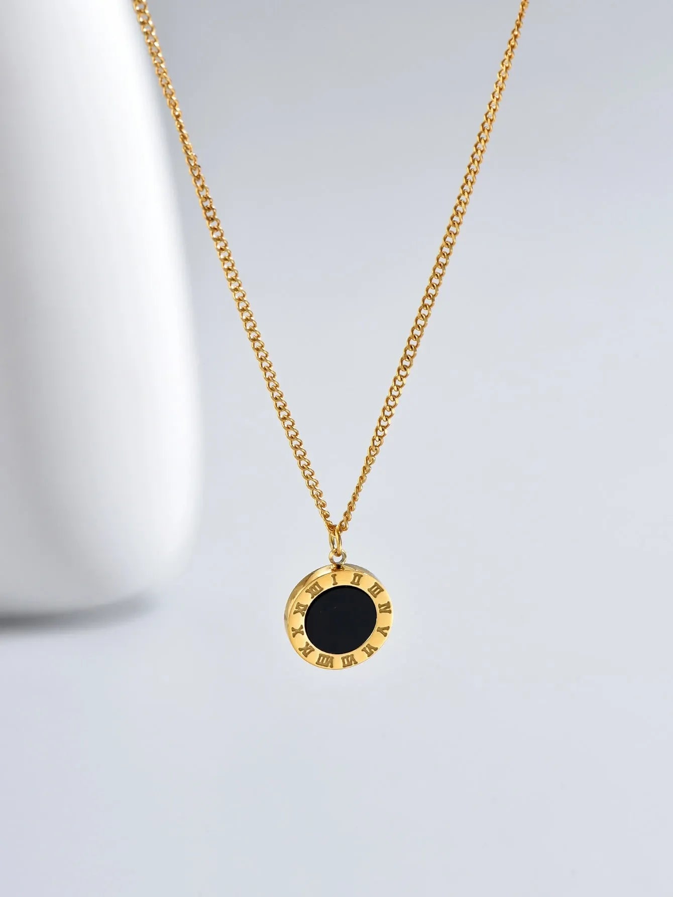 Gold necklace with a black pendant on a light gray background
