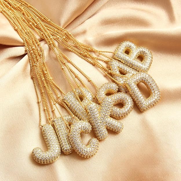 Gold necklaces with letter pendants on a beige fabric background