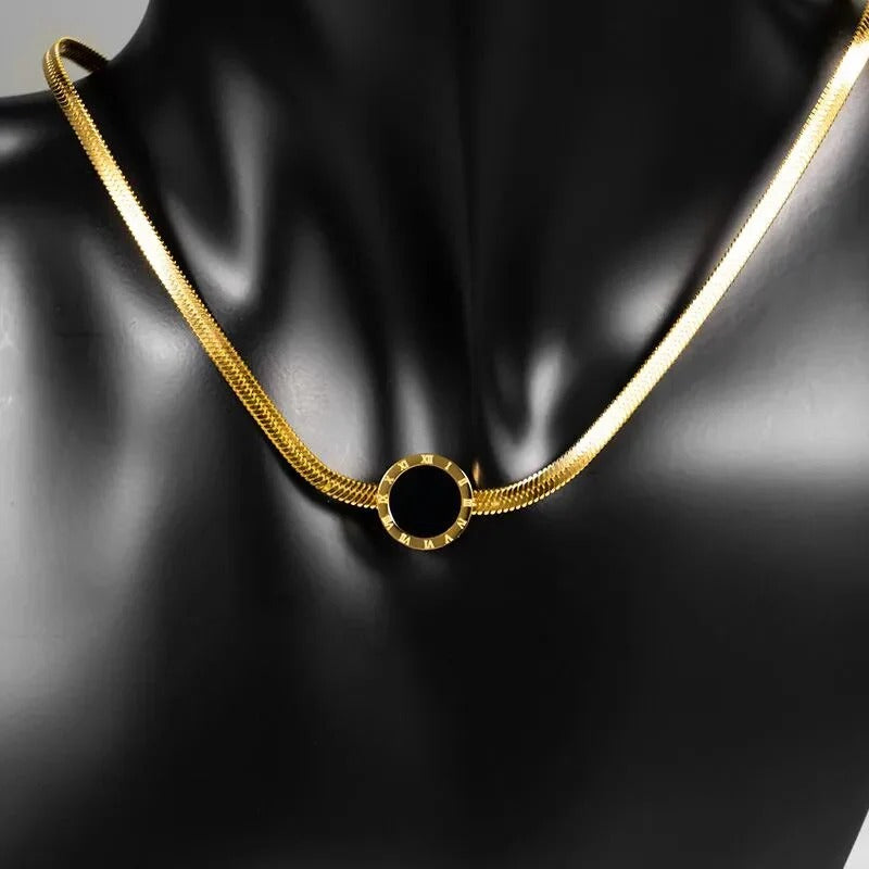 Gold necklace with a black circular pendant on a black mannequin.
