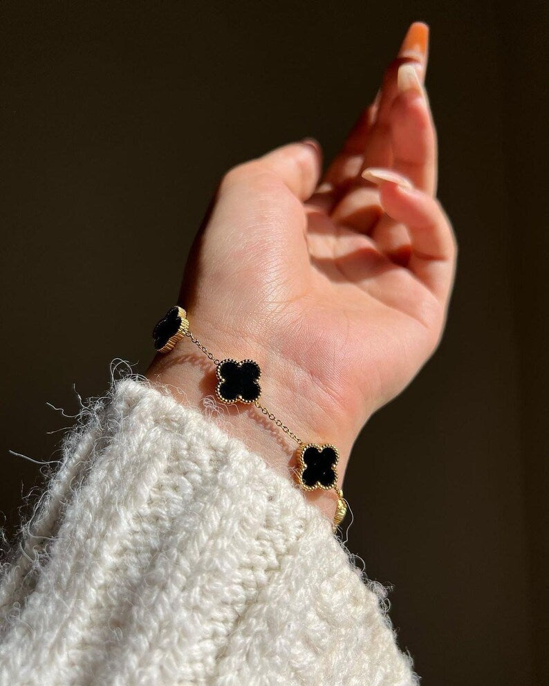 Hand wearing a bracelet with black clover-shaped charms against a blurred background