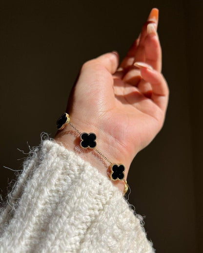 Hand wearing a bracelet with black clover-shaped charms against a blurred background