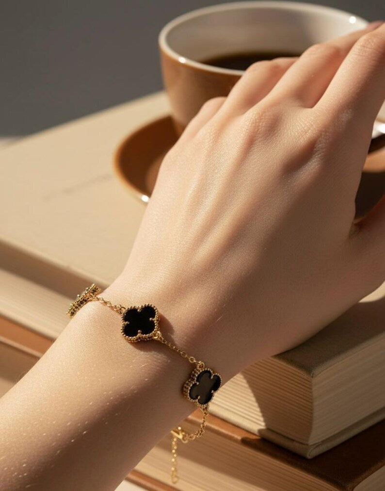 Hand wearing a gold bracelet with black stones on a wooden surface with a cup of coffee.