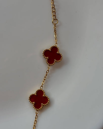 Gold necklace with maroon clover pendants on a light gray background