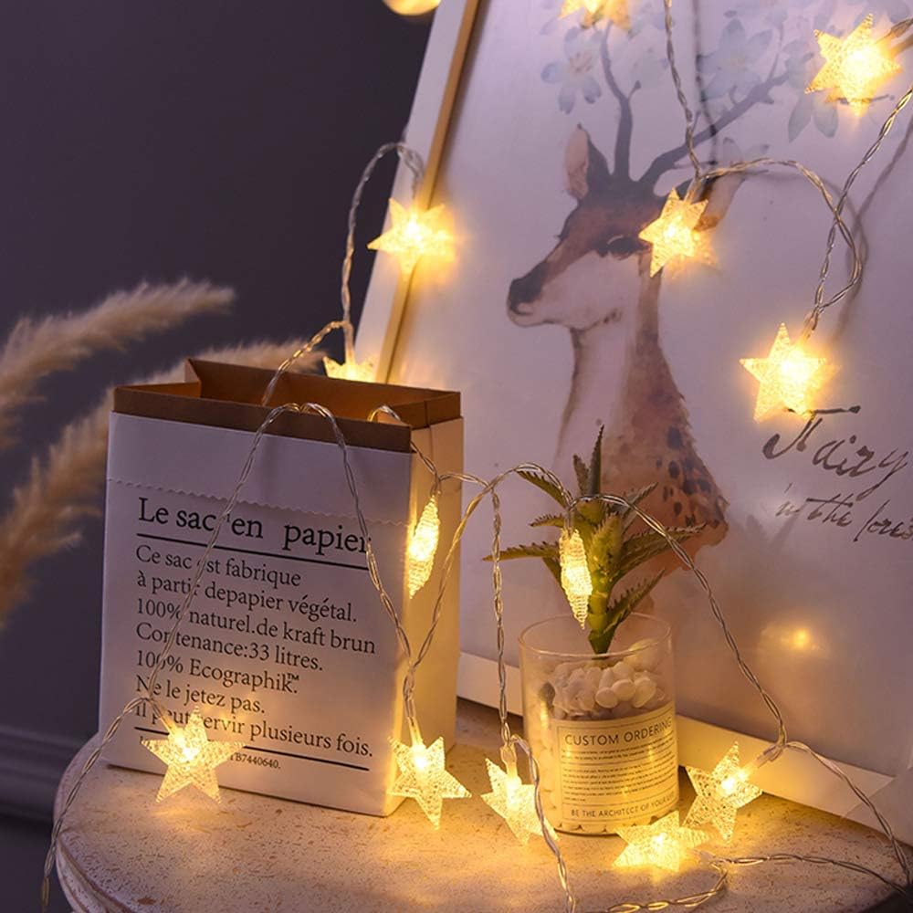 Decorative string lights with star-shaped bulbs on a table with a plant and a glass.