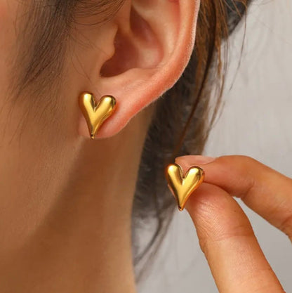 Gold heart-shaped earrings worn by a person with a neutral background