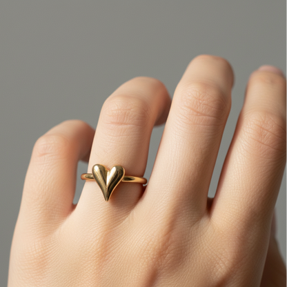 Gold heart-shaped ring on a person's finger against a neutral background