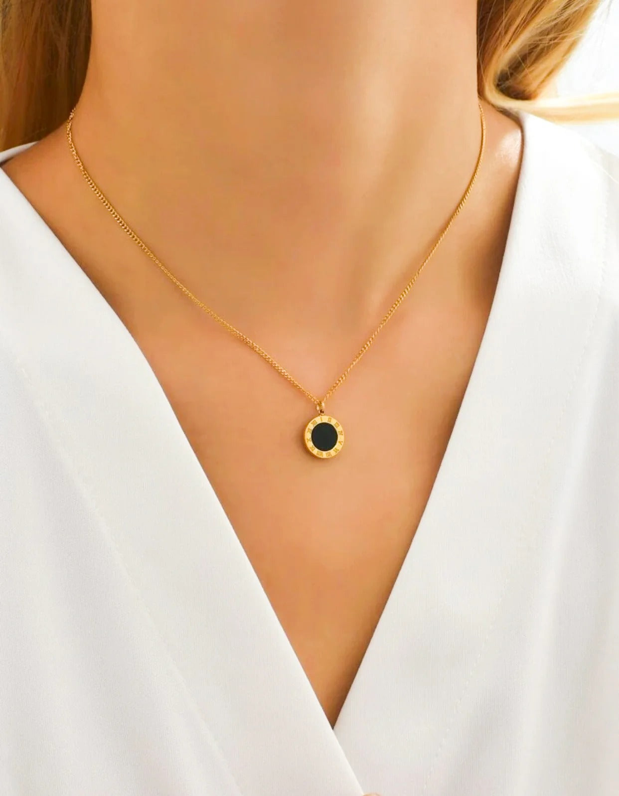 Gold necklace with a black pendant on a person wearing a white top.