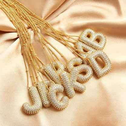 Gold necklaces with letter pendants on a beige fabric background