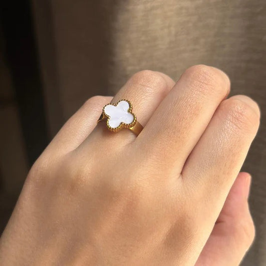 Gold ring with a white stone on a person's finger against a neutral background