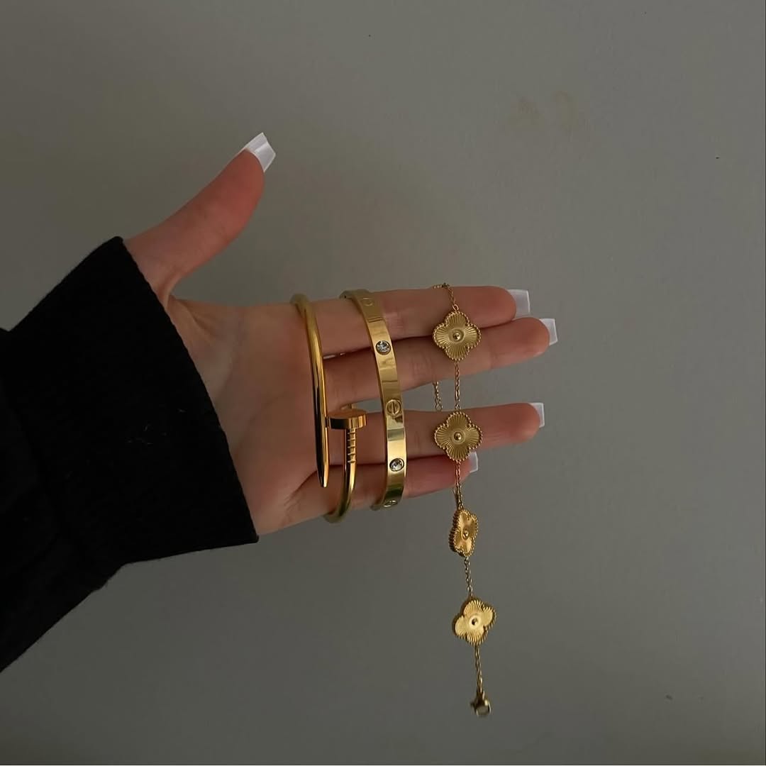 Hand wearing gold bracelets and a gold ring with a pendant on a plain background