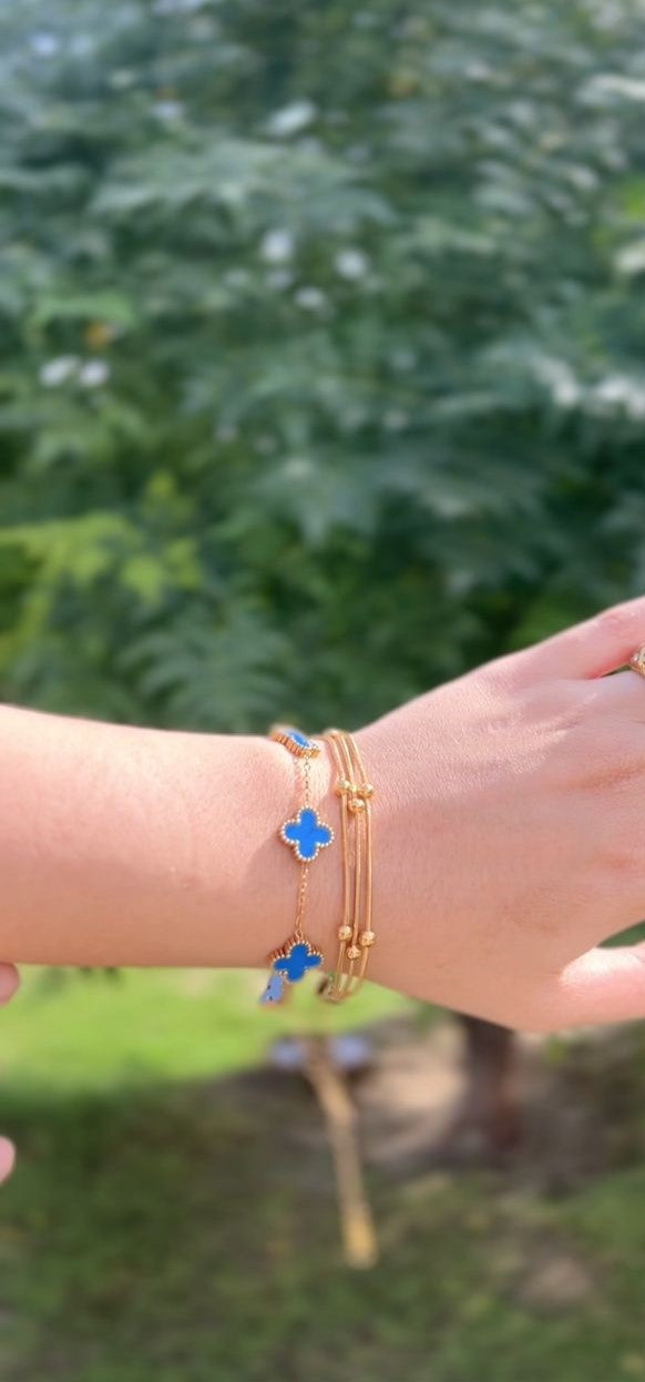 Hand wearing multiple bracelets with blue flower designs against a blurred green background