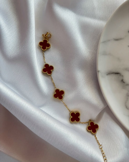 Gold bracelet with maroon clover-shaped charms on a white fabric background