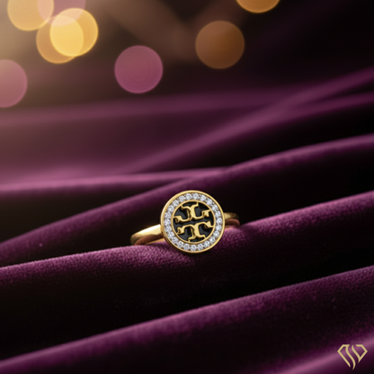 Gold ring with a circular design on a purple fabric background
