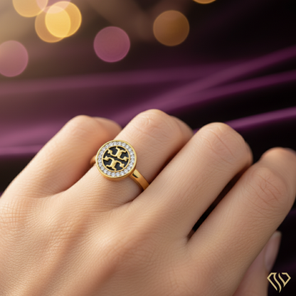 Gold ring with a black and white design on a hand against a blurred purple fabric background